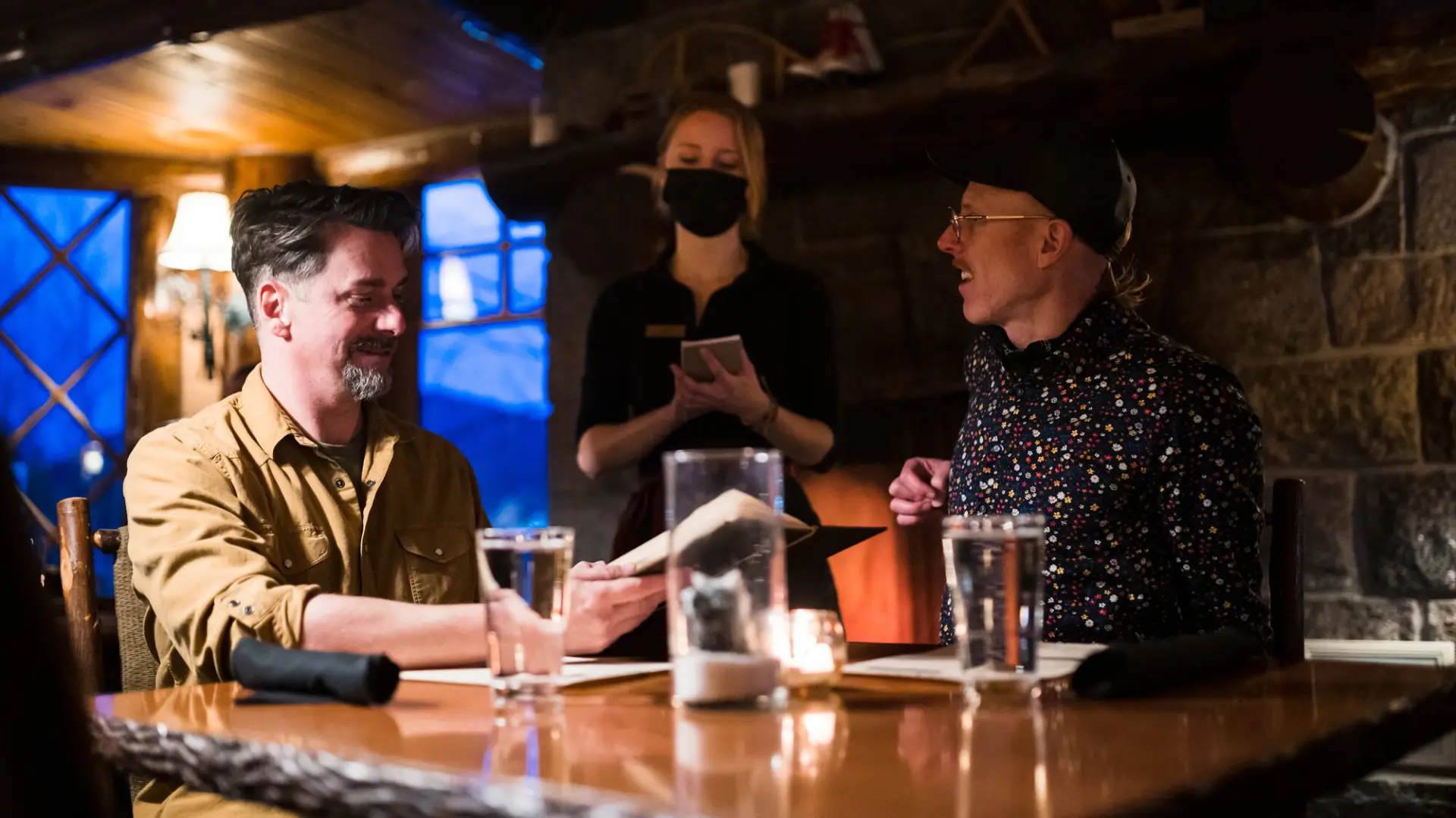 Two men smile while ordering food at a romantic, dimly lit restaurant.