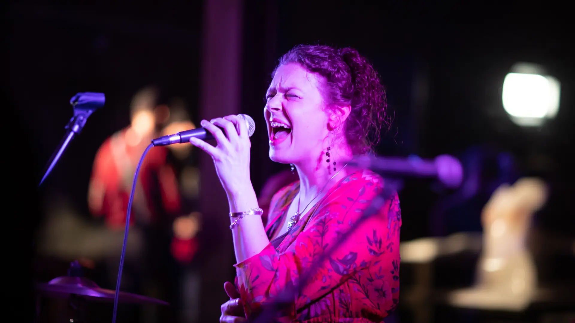 Woman in long sleeve red dress sings into microphone on dark stage