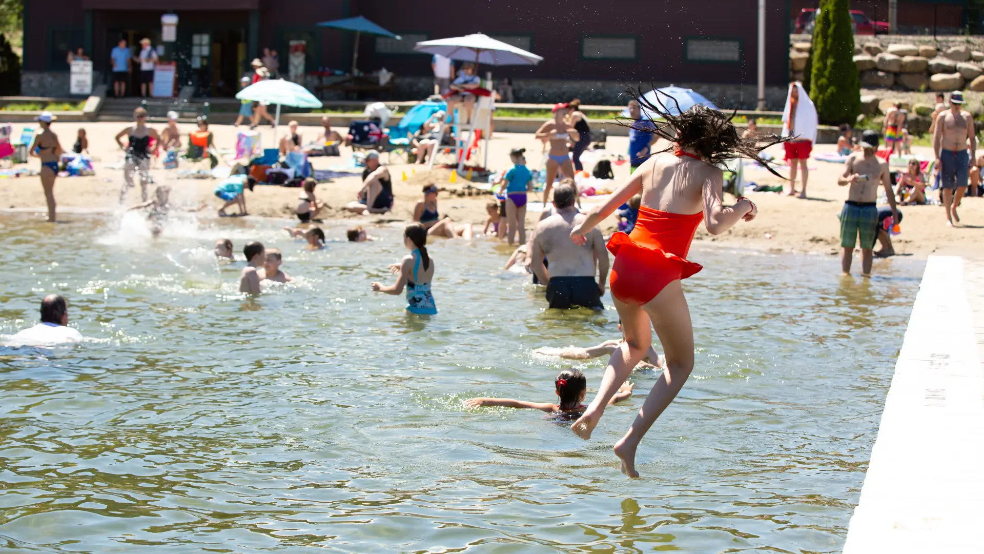 People swimming at the beach and jumping off a dock.