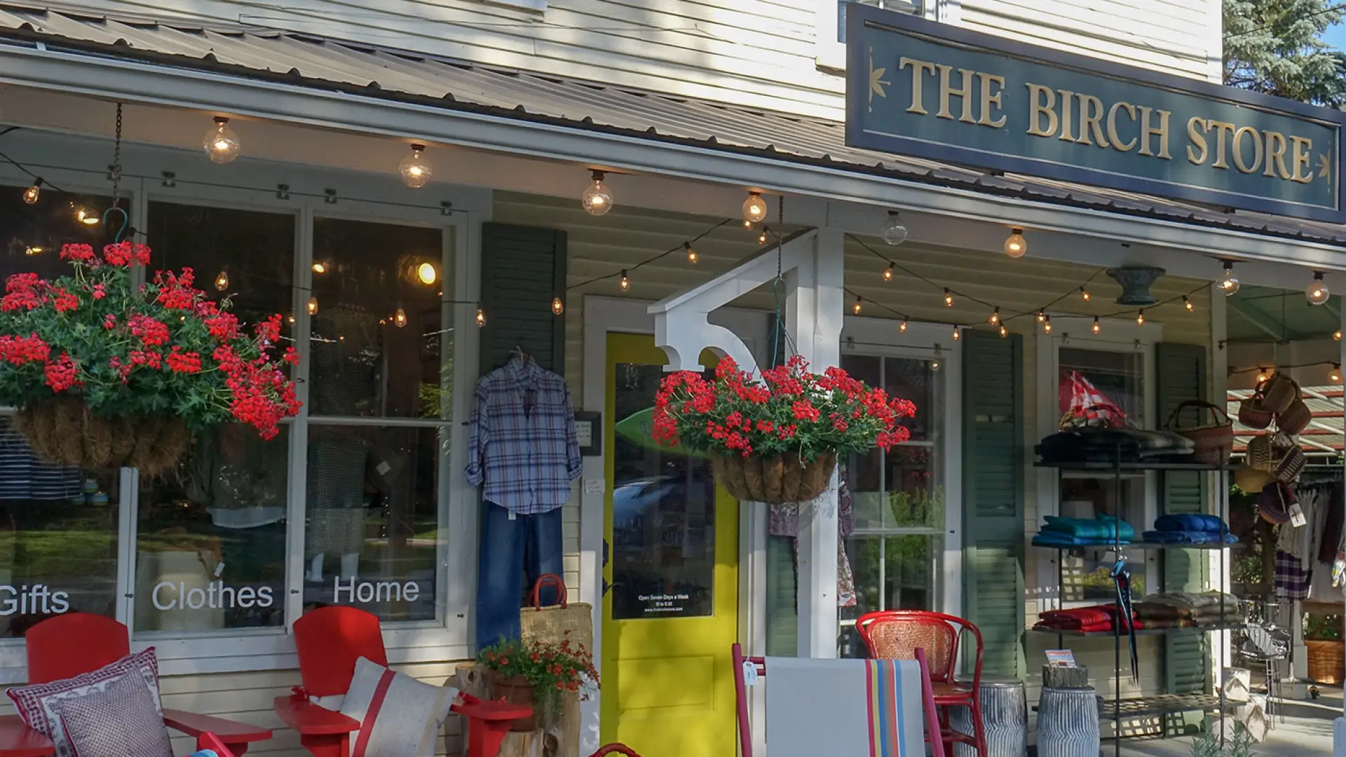The exterior of The Birch Store decorated for the summer season with brightly colored lawn chairs and hanging flower baskets