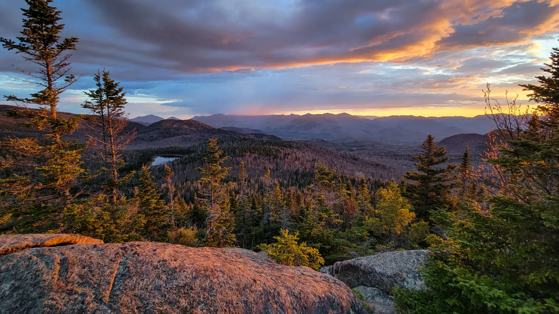 A mountainous view with a small pond at sunset