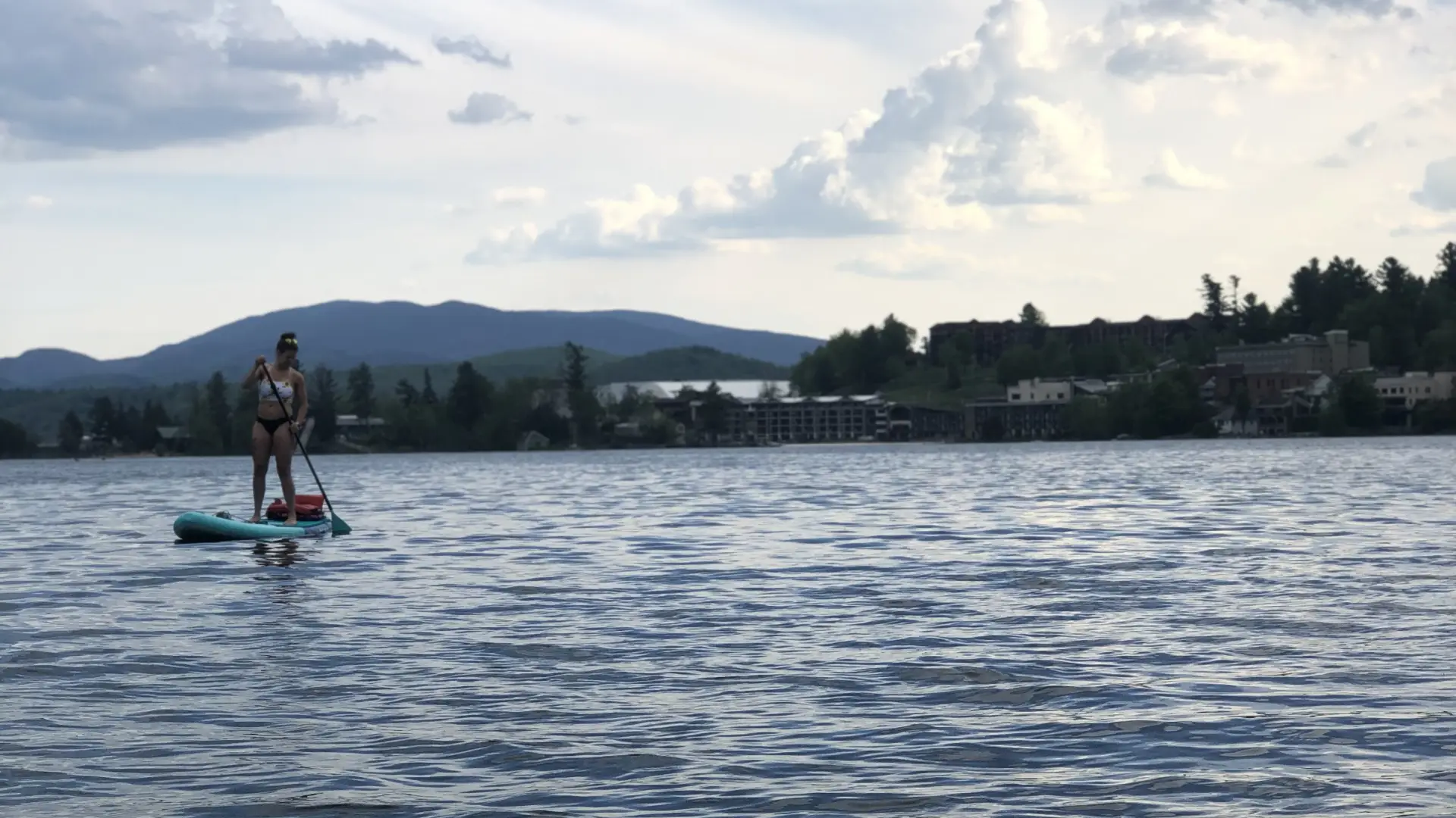 A woman paddles a SUP on a lake with mountains and trees in the background.