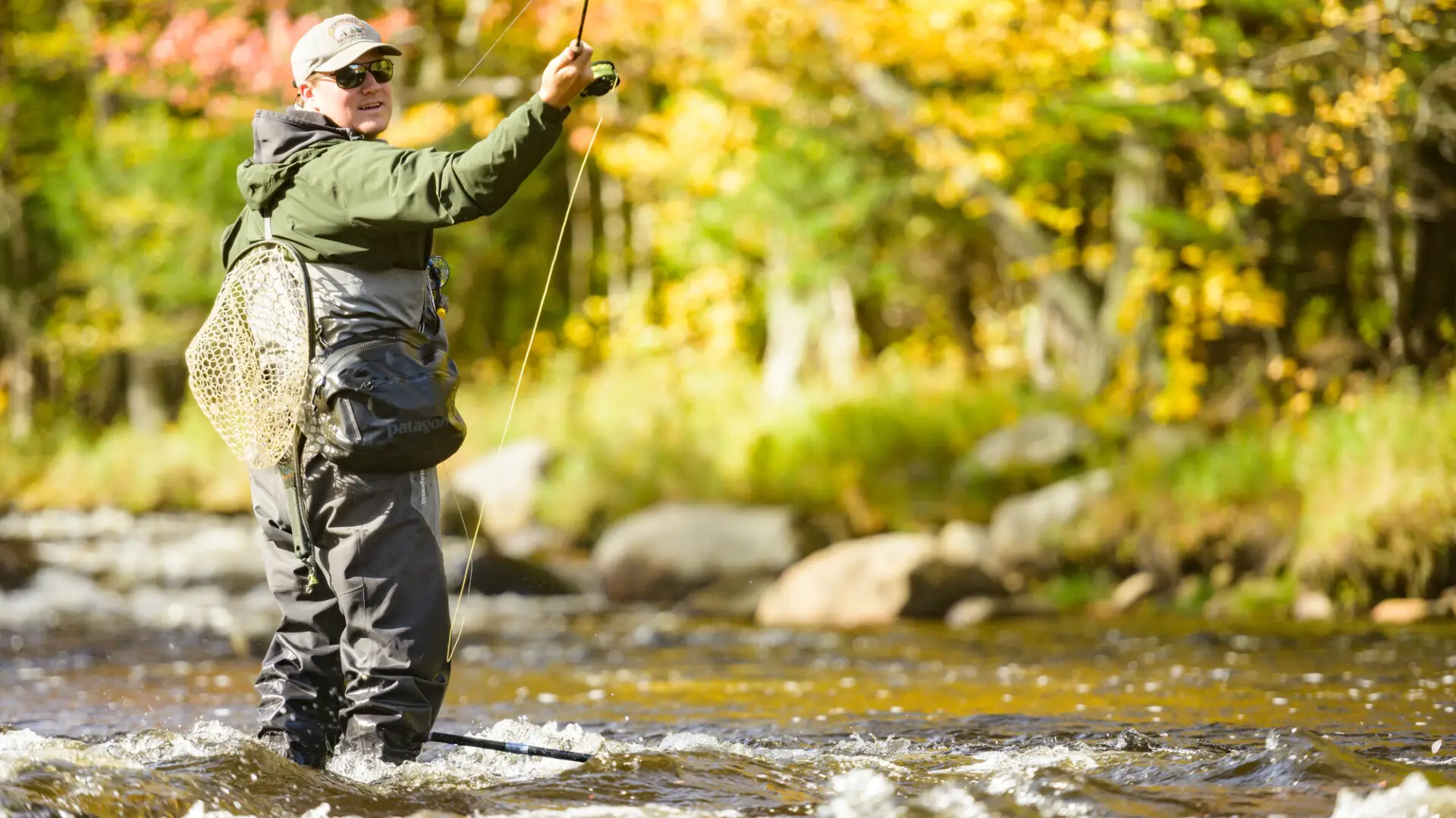 A man casts his line into the Au Sable River with bright fall foliage in the background