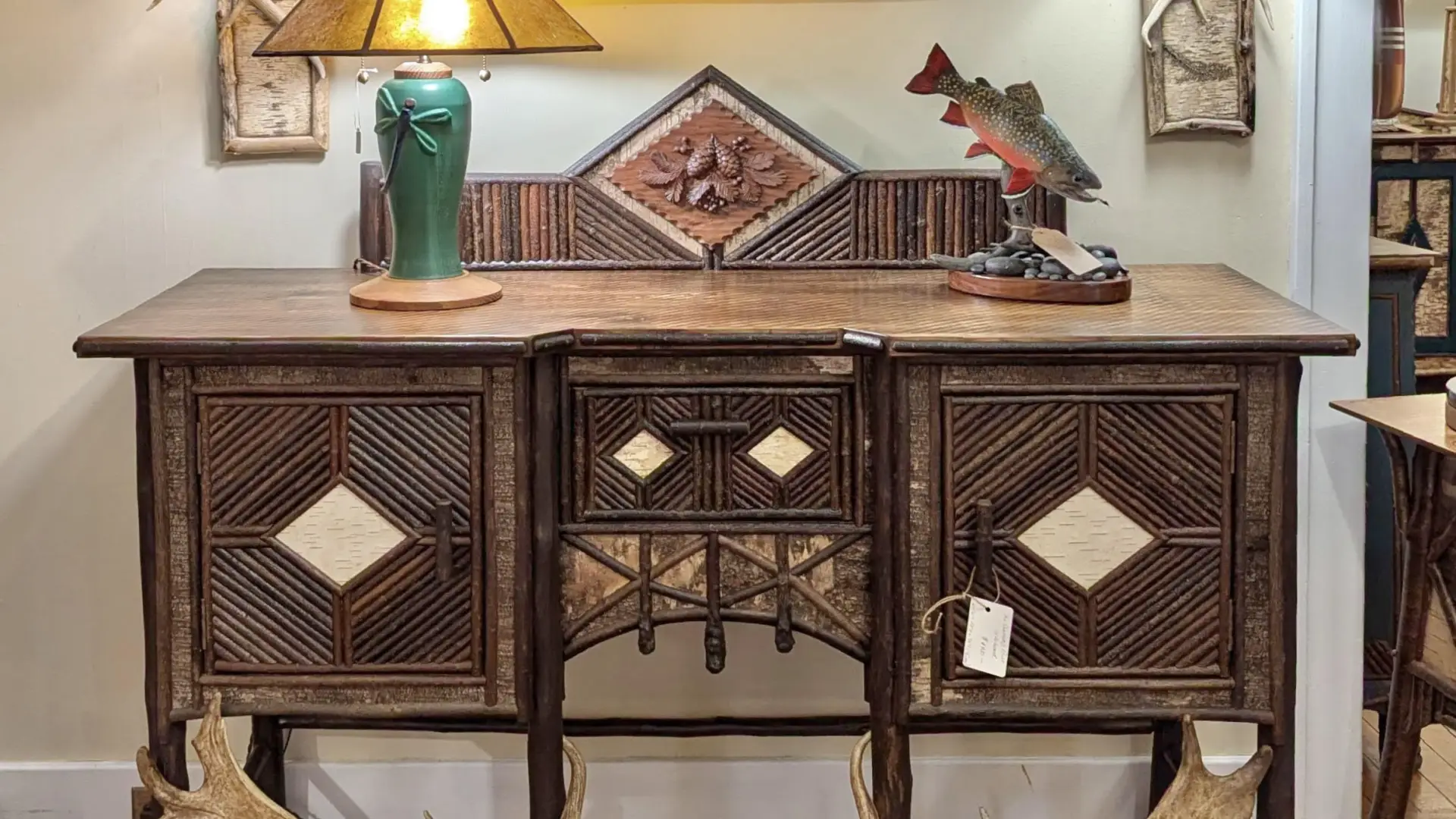 A rustic buffet table decorated with twig work and antlers, and a painting of salmon among a rocky stream bed in a matching twig frame.
