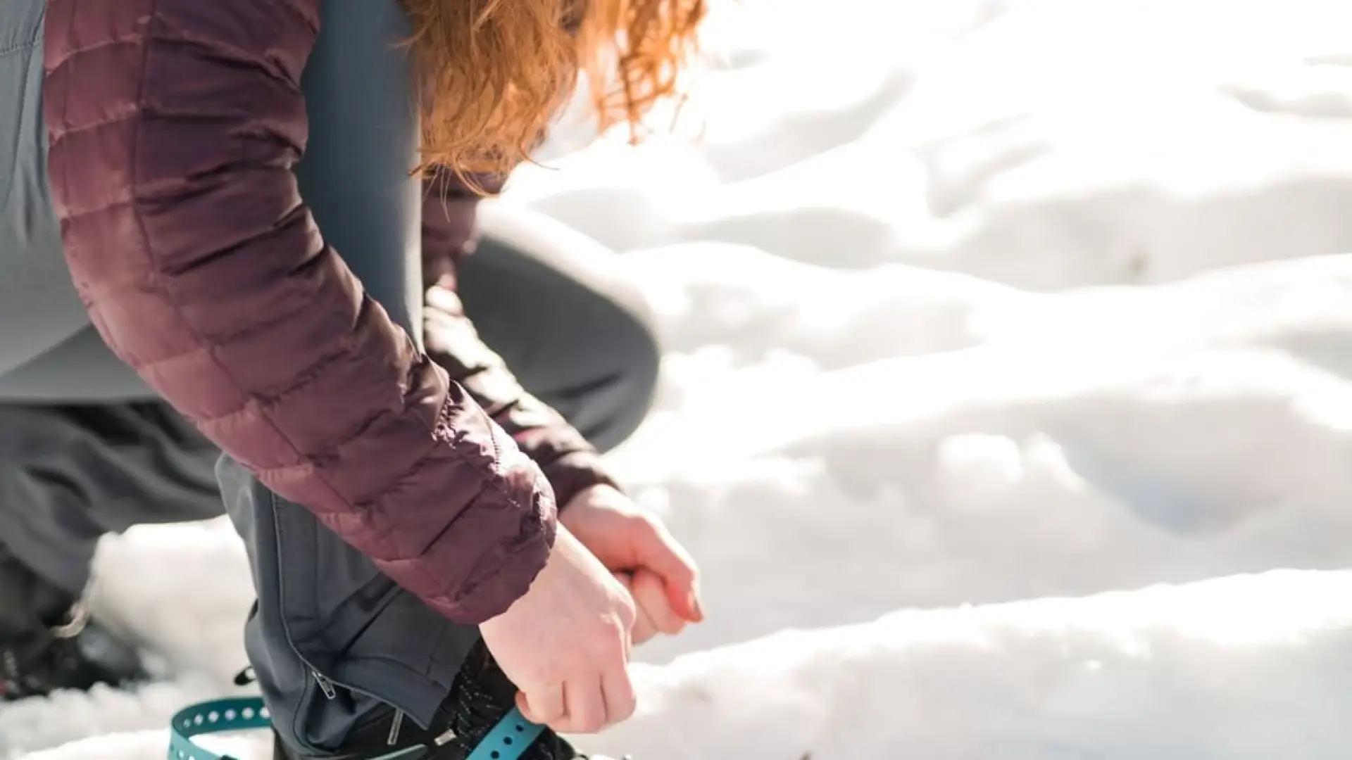 A red haired person adjusts the straps on her snowshoe