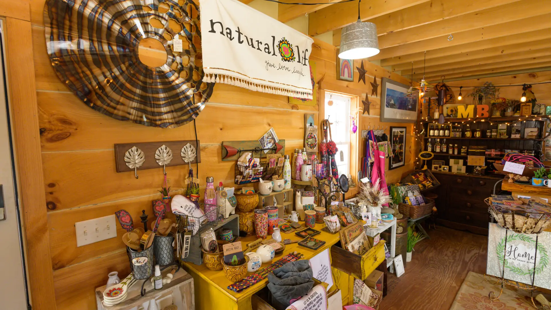 Colorful decor items, mugs, water bottles and kitchen utensils sit atop a yellow dresser in front of knotty pine walls