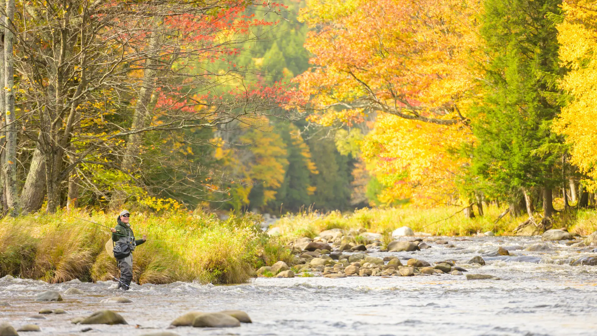 A man smiling while fly fishing and standing in the Ausable River.