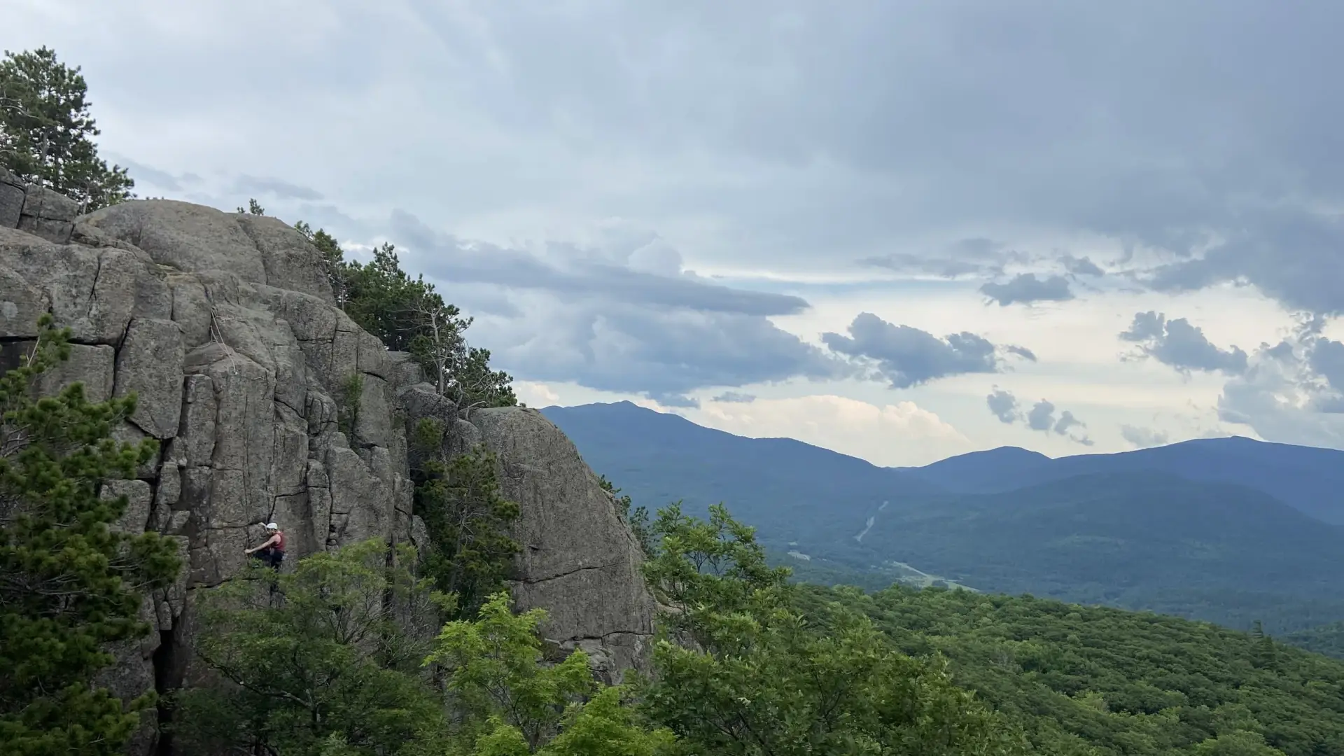 Mountain background while person climbs a shear cliff face in the forground