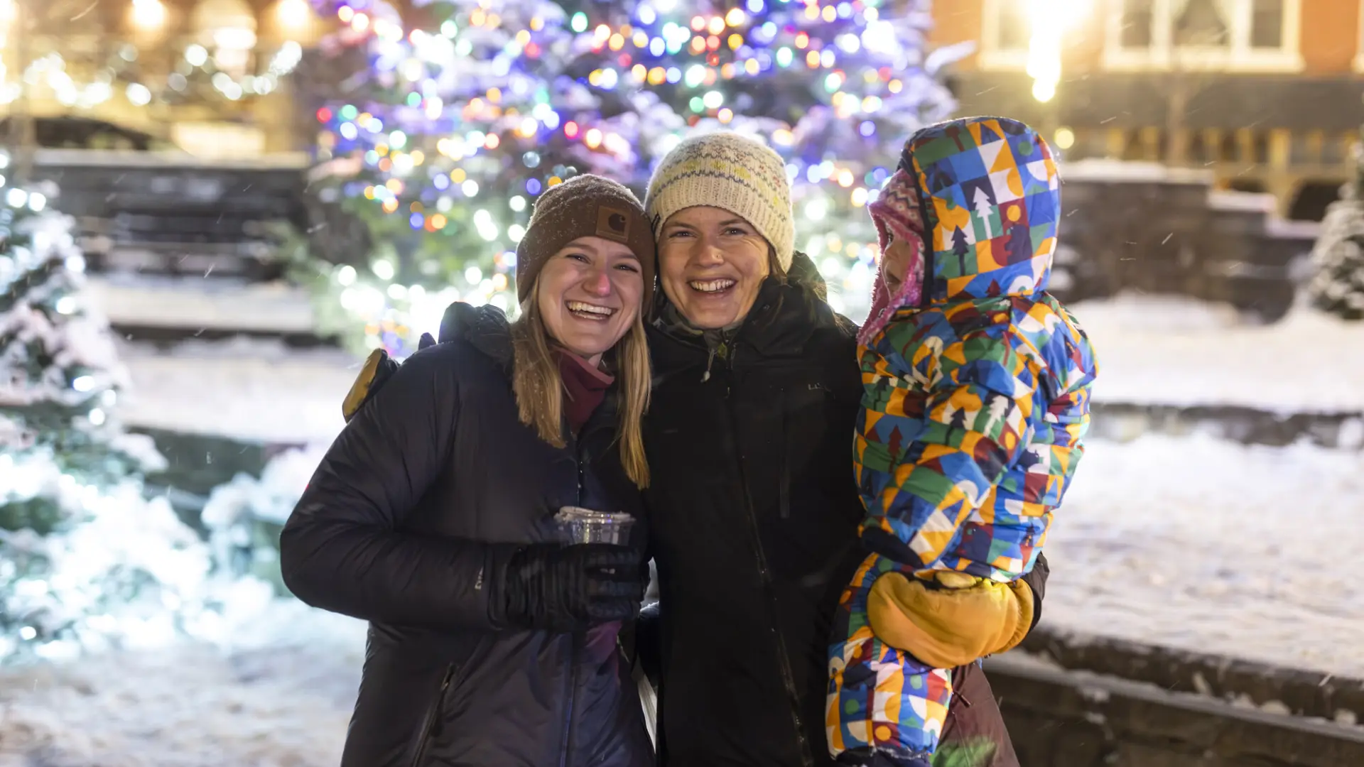 A group of people having posing for a picture in front of the Christmas tree out in the park.