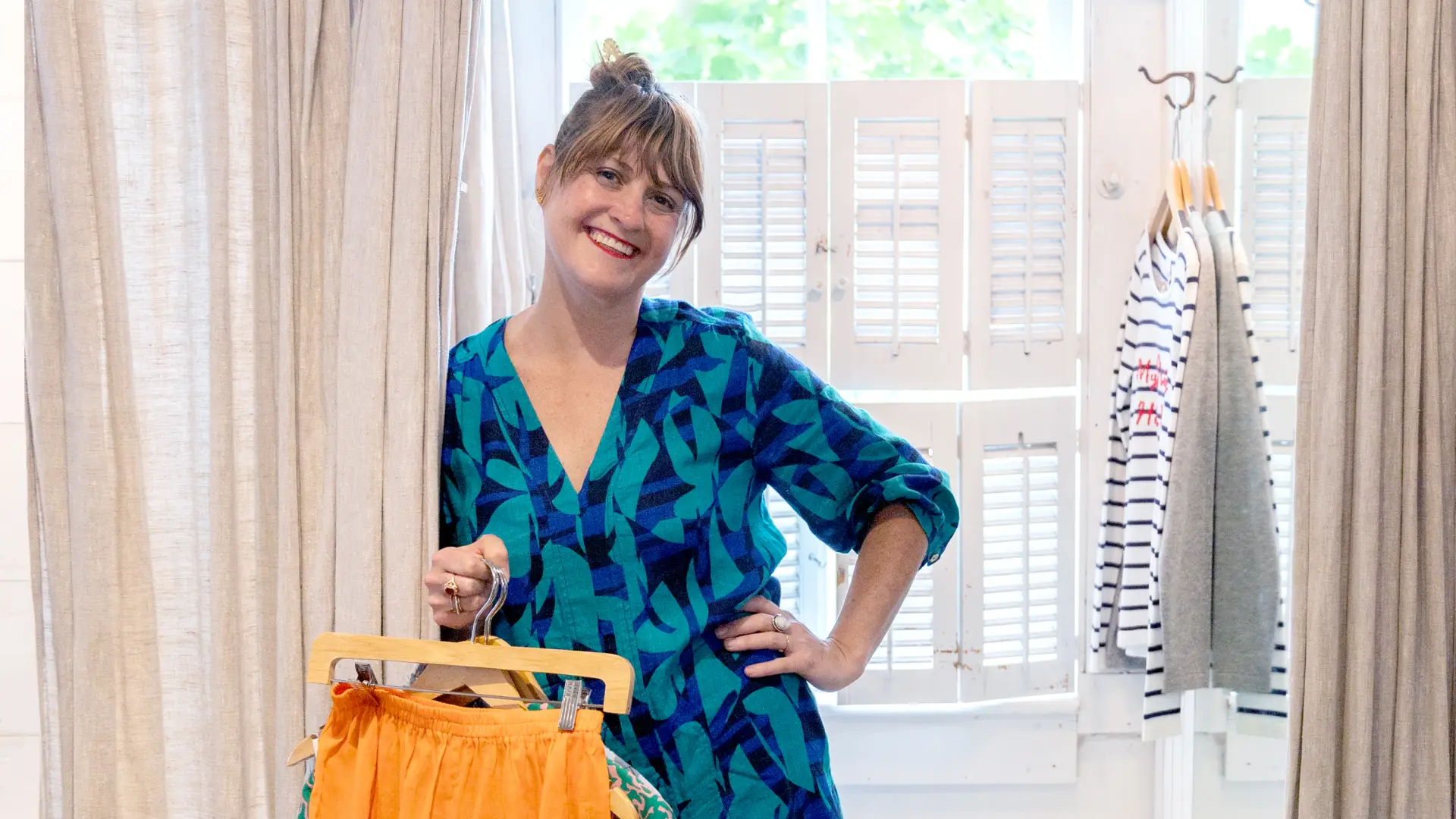 A happy lady in a blue dress stepping out of the dressing room with her winning clothing choices.