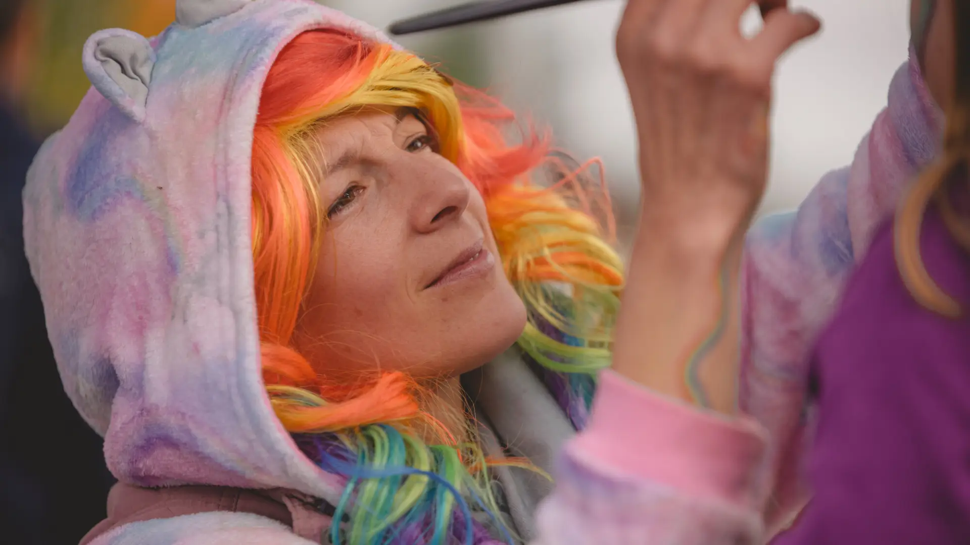 Woman with colorful hair paints a childs face at the fall festival.