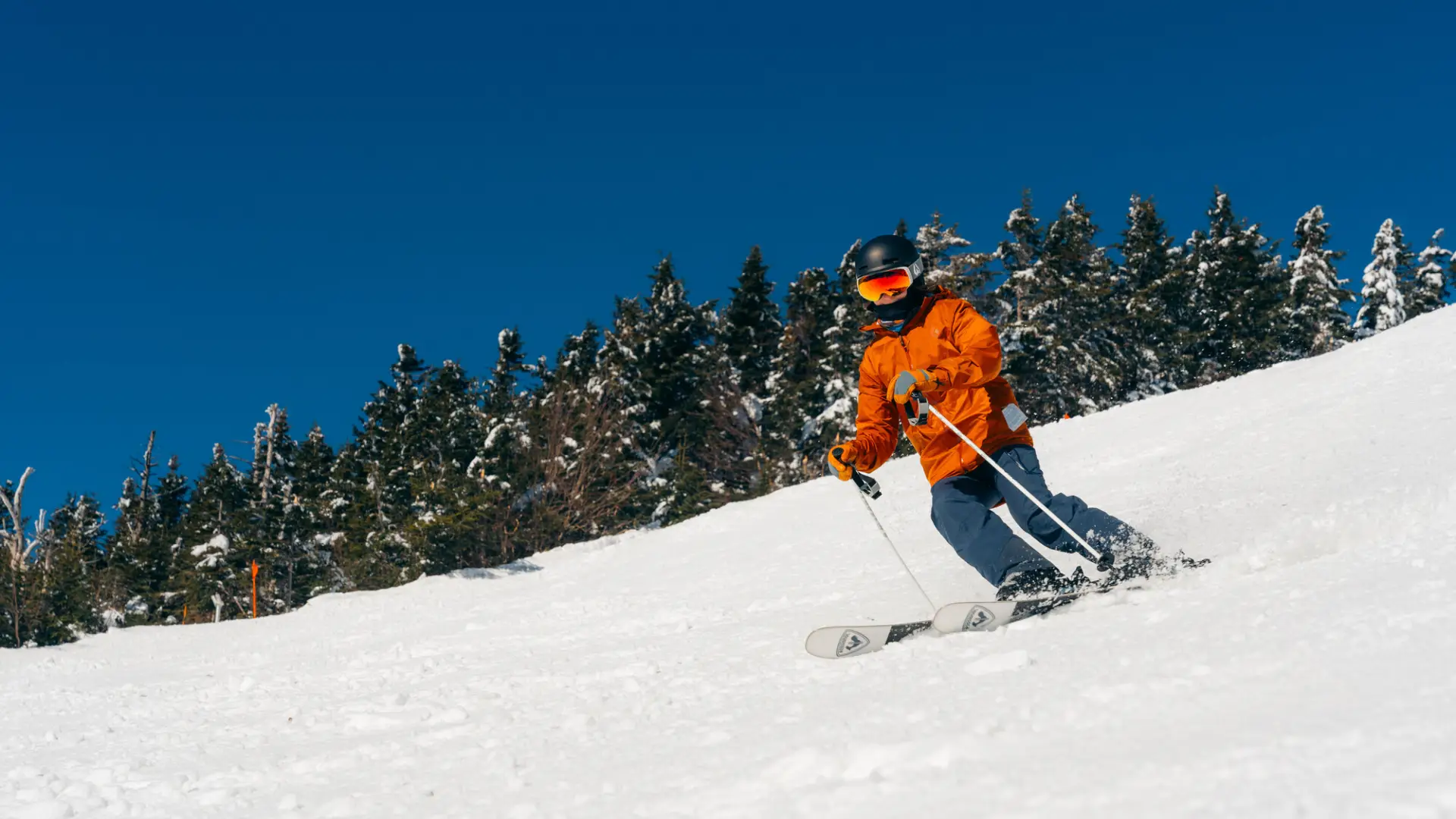 A skier in an orange jacket races down a mountain.