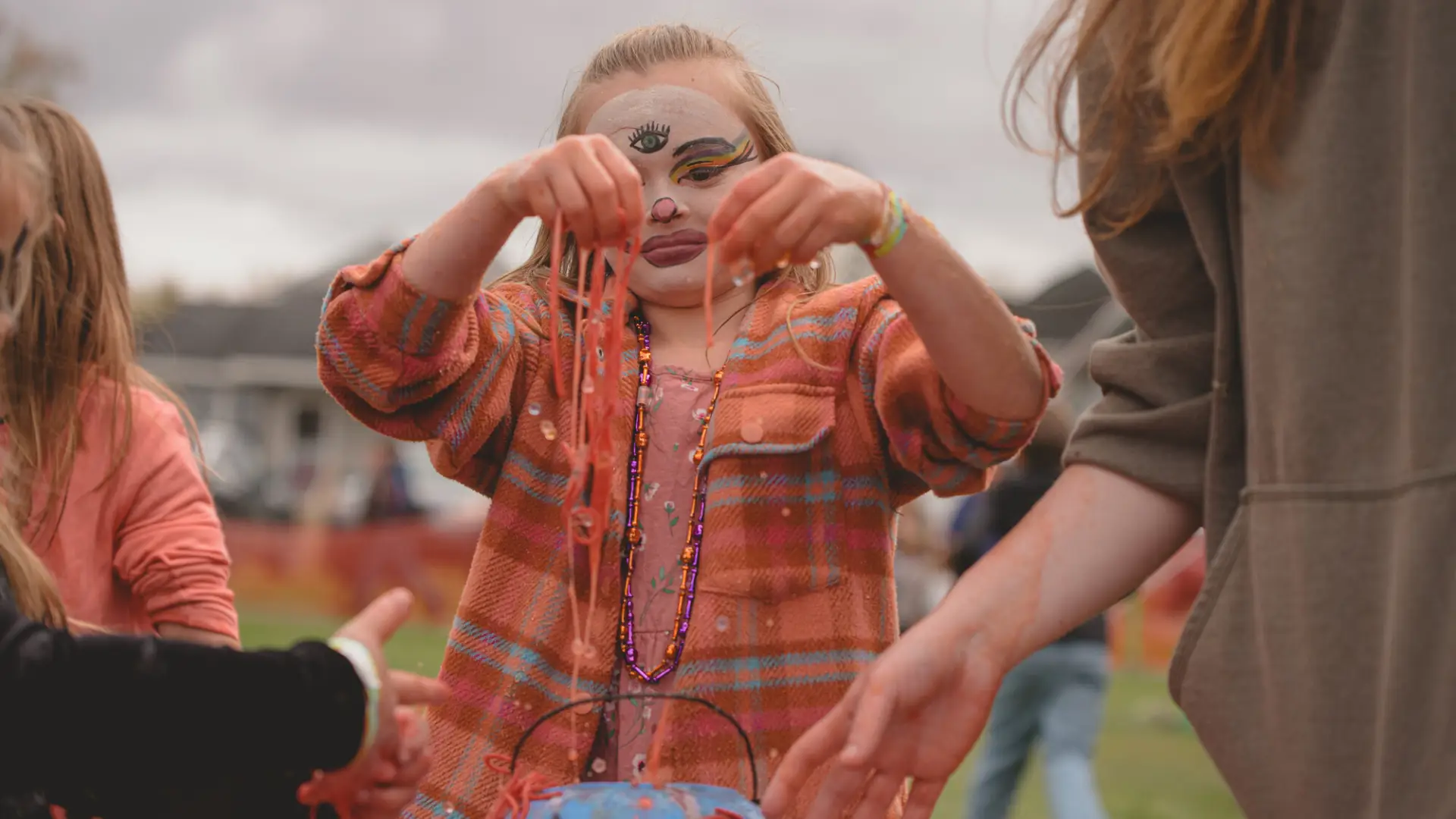 Child with face painted at Tupper's fall festival holds up necklaces.