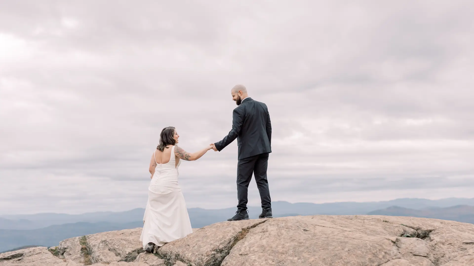 Bride and groom laugh atop a rocky knoll 