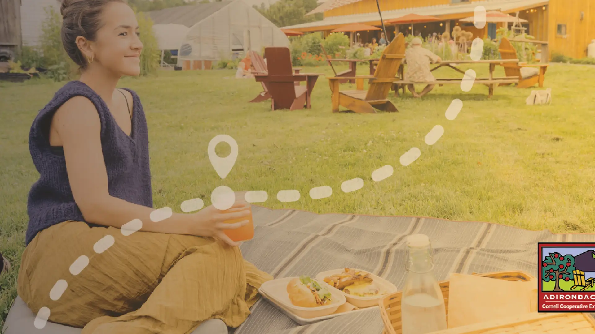 A woman sits on a blanket at an outdoor restaurant and has a picnic. 