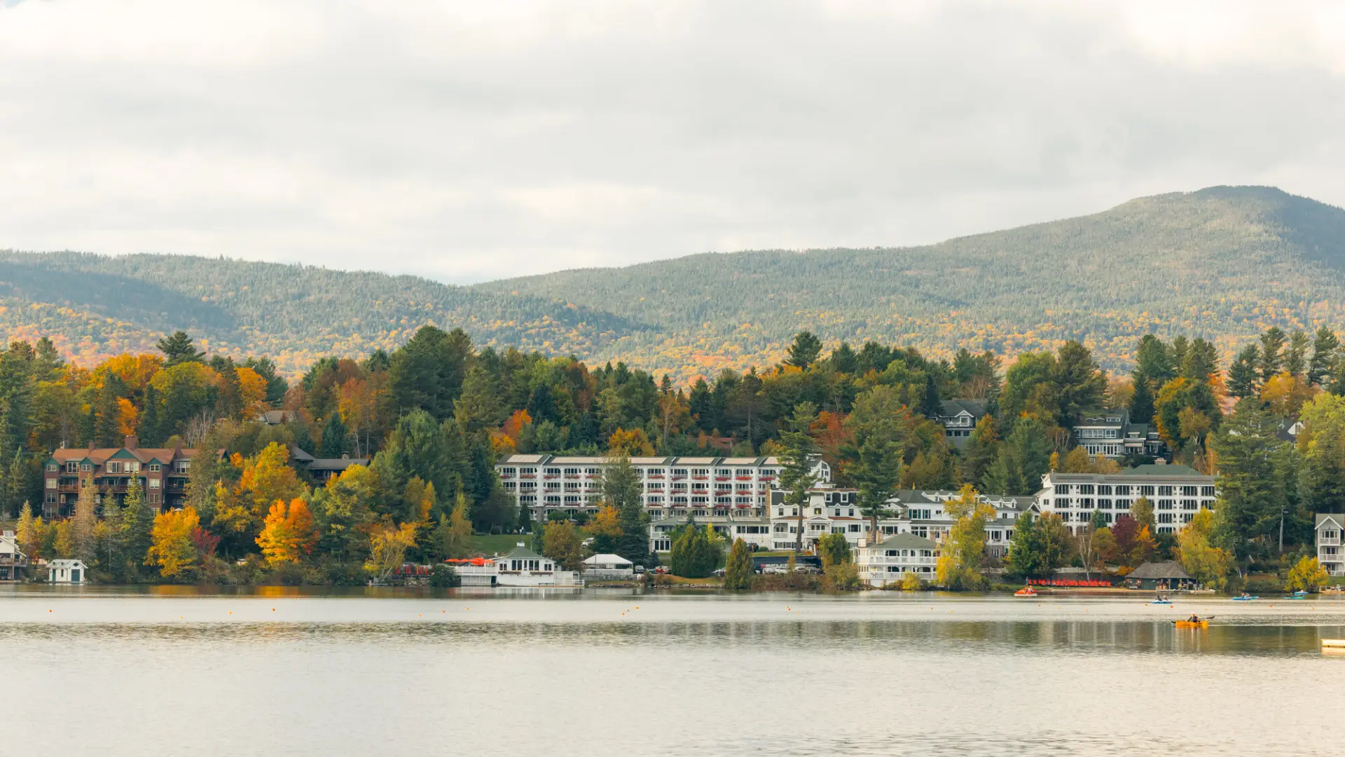 Hotels in downtown Lake Placid seen from across lake with fall foliage mountains in background