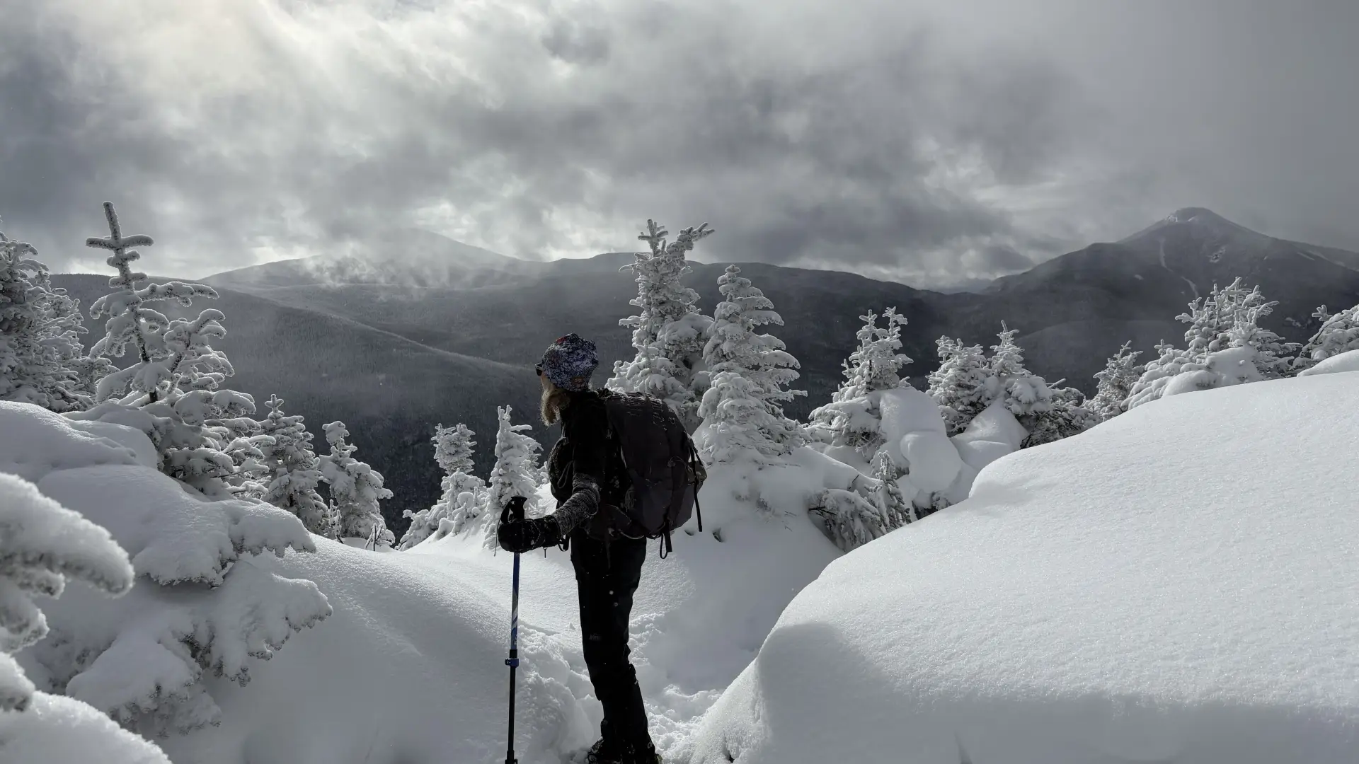 Snowshoer takes in the mountains in the distance, surrounded by pillows of beautiful snow and encrusted trees at the top of a peak