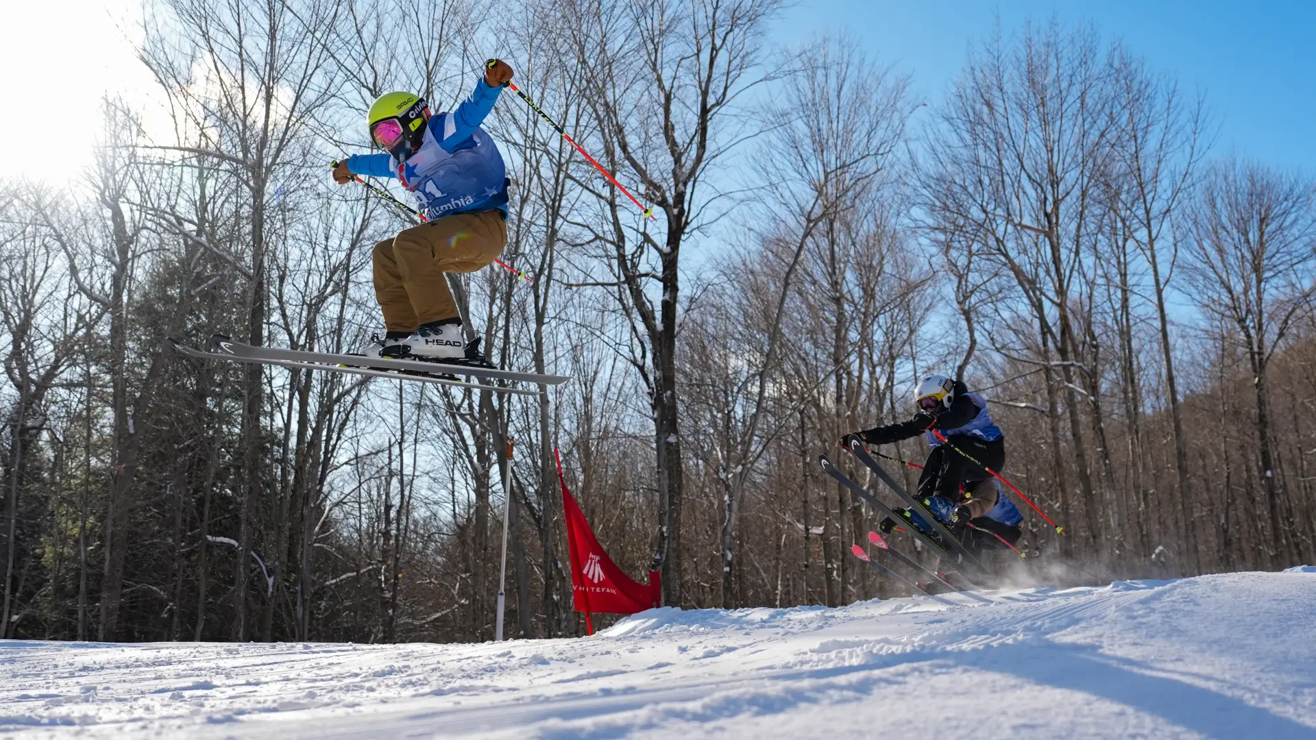 Three skiers wearing competition bibs catch air simultaneously during a cross race at Whiteface Mountain.