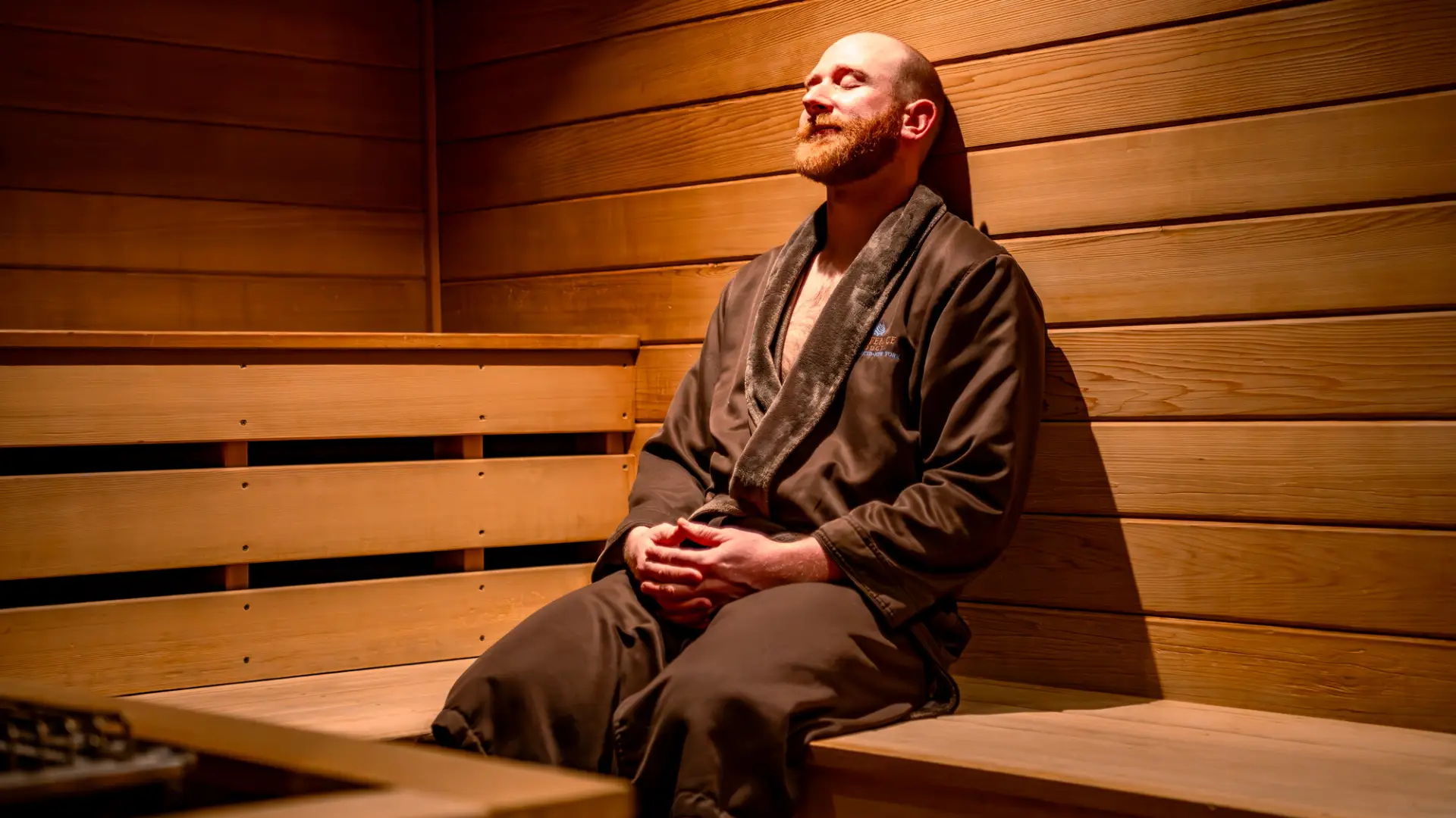A man wearing a spa robe relaxes with his eyes closed in a sauna