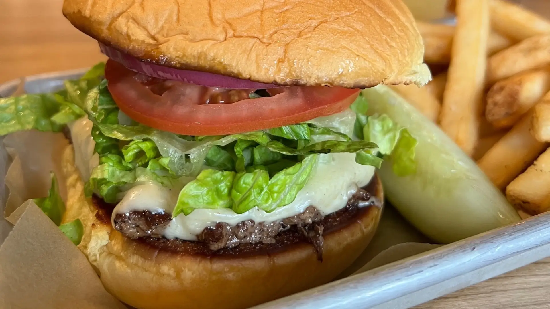 Cheese burger with thick slice of tomato and shredded lettuce with french fries, a pickle wedge and a freshly poured beer