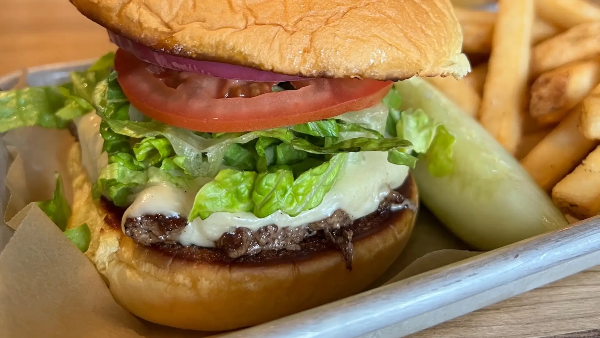 Cheese burger with thick slice of tomato and shredded lettuce with french fries, a pickle wedge and a freshly poured beer