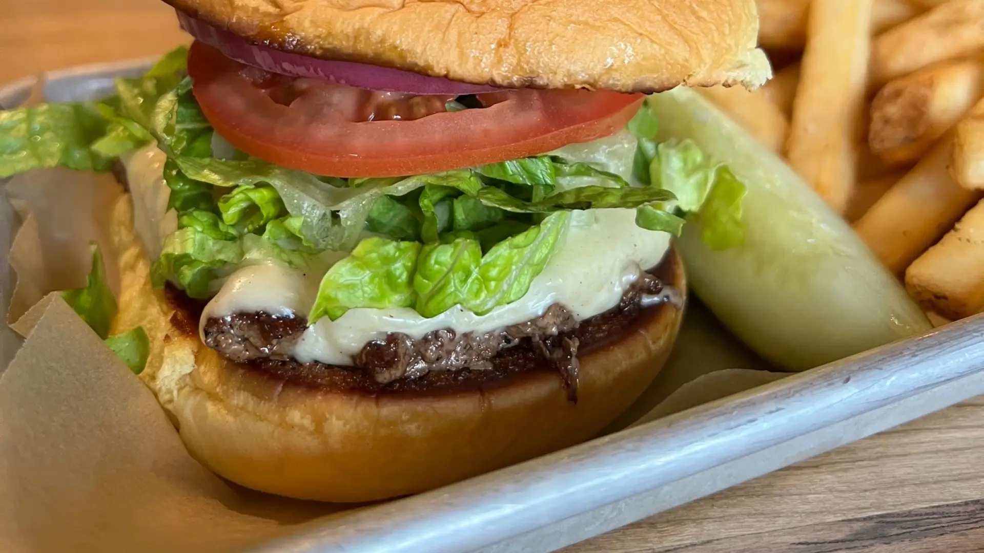 Cheese burger with thick slice of tomato and shredded lettuce with french fries, a pickle wedge and a freshly poured beer