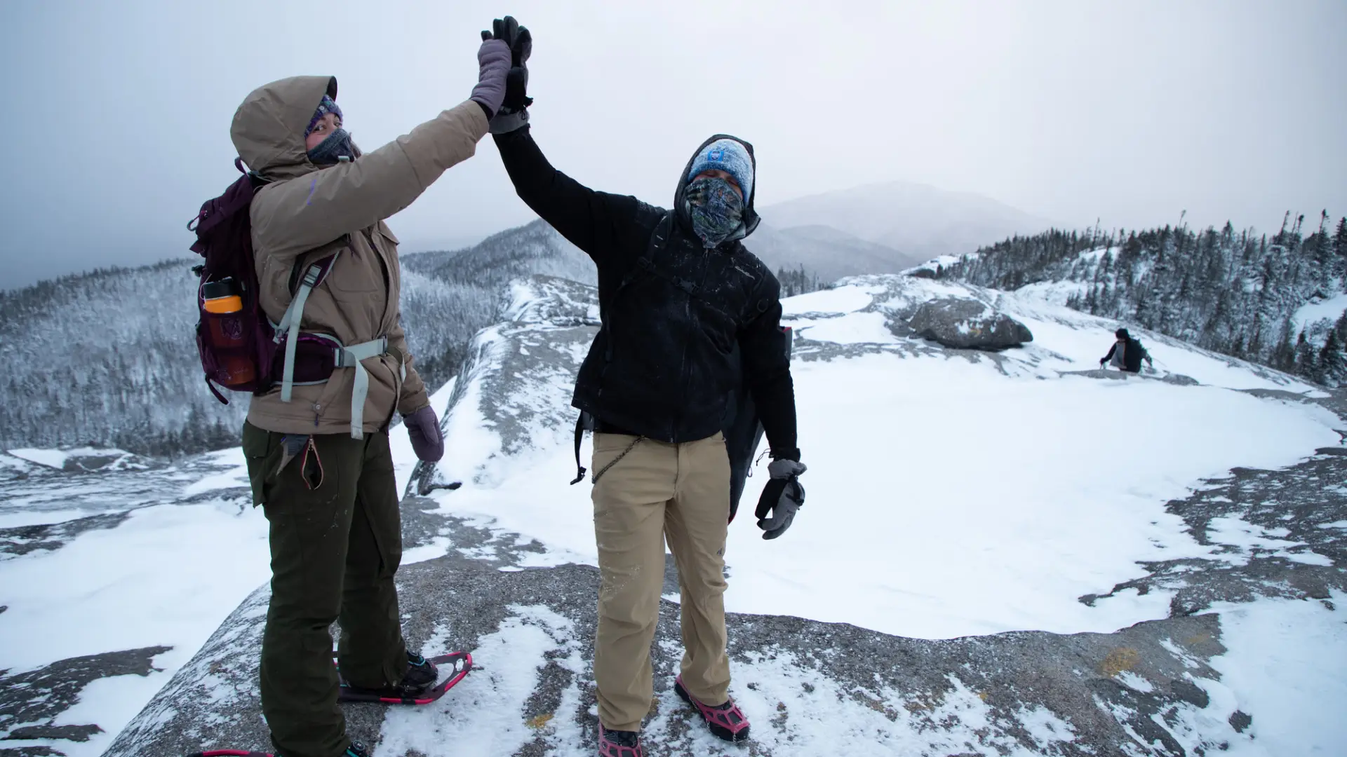 Two people high five on a snowy peak, Ampersand Mountain.