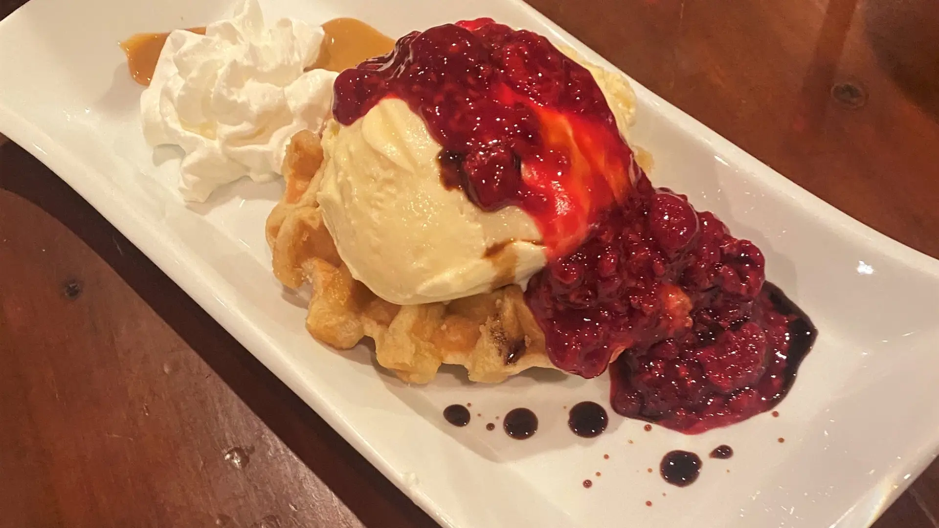 A lavish dessert of waffle, ice cream, caramel, and raspberry sauce.