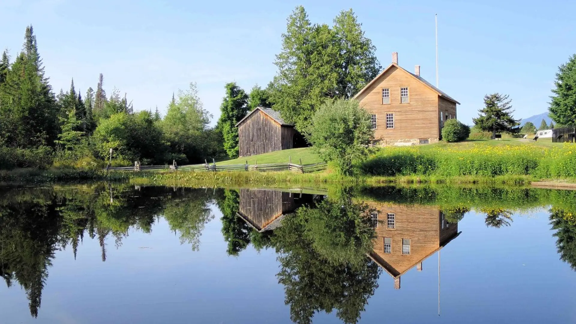 John Brown's house at John Brown Farm seen over and reflecting in a placid pond in summertime