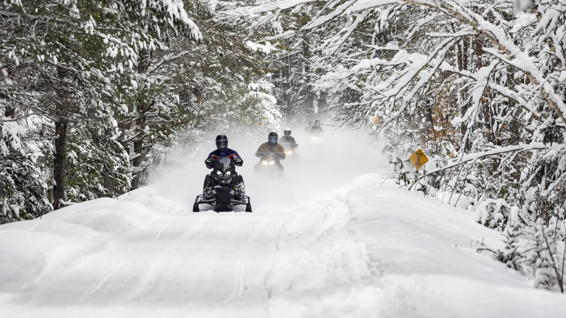 Snowmobiles ride in a line on a snowy trail