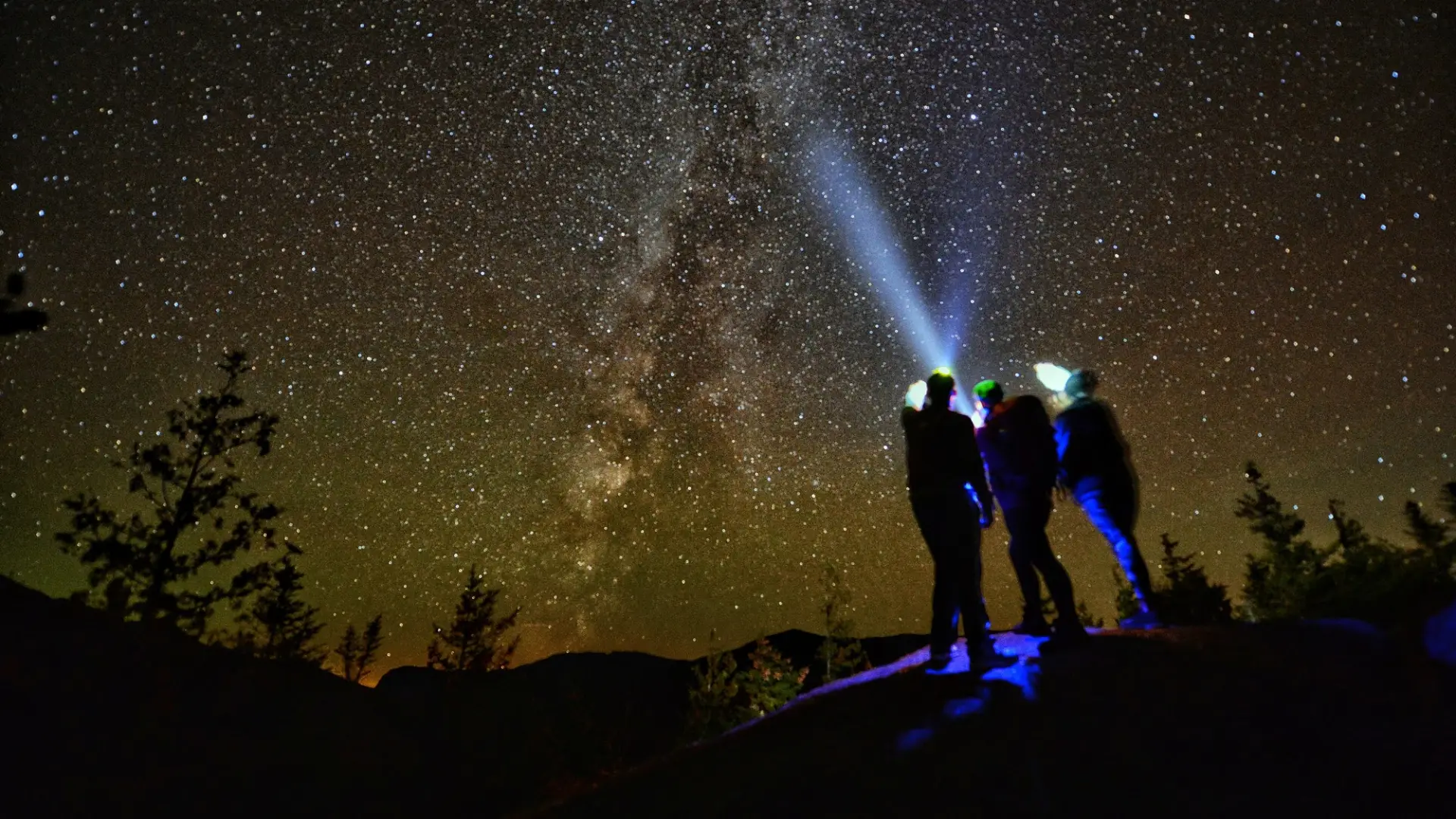 Three hikers stargazing at a summit.