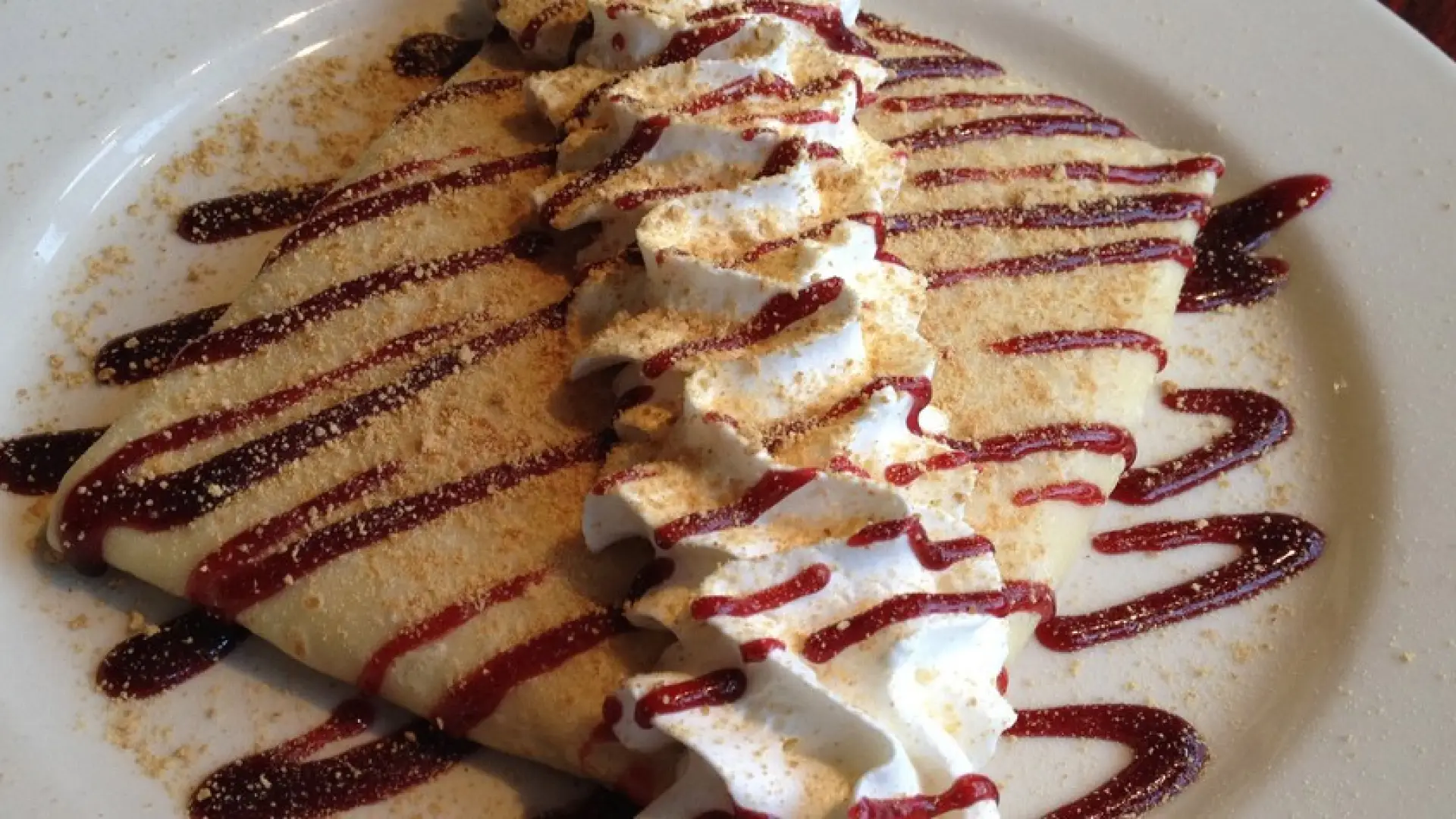 A crepe with whipped cream and strawberry jam striped on top.