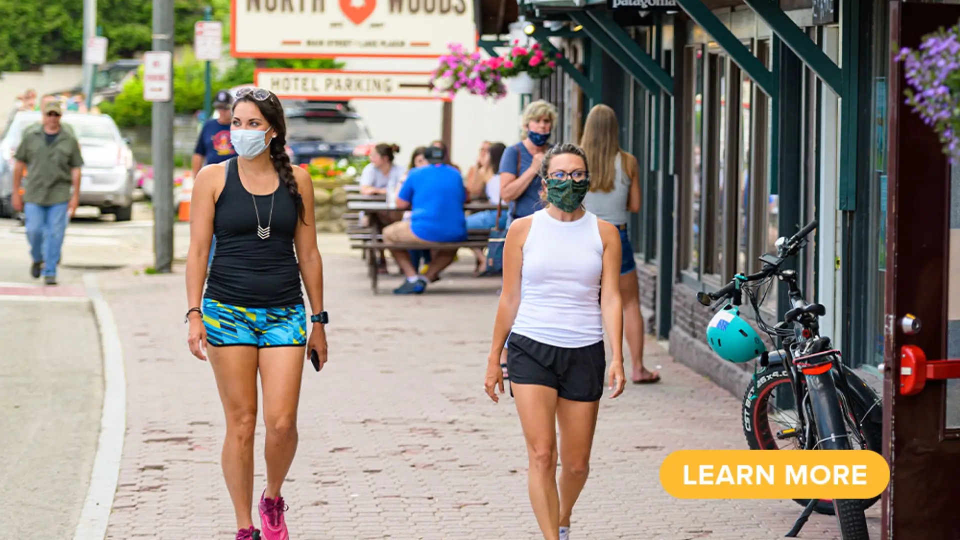 Two women stroll Main Street in masks and summer clothing.