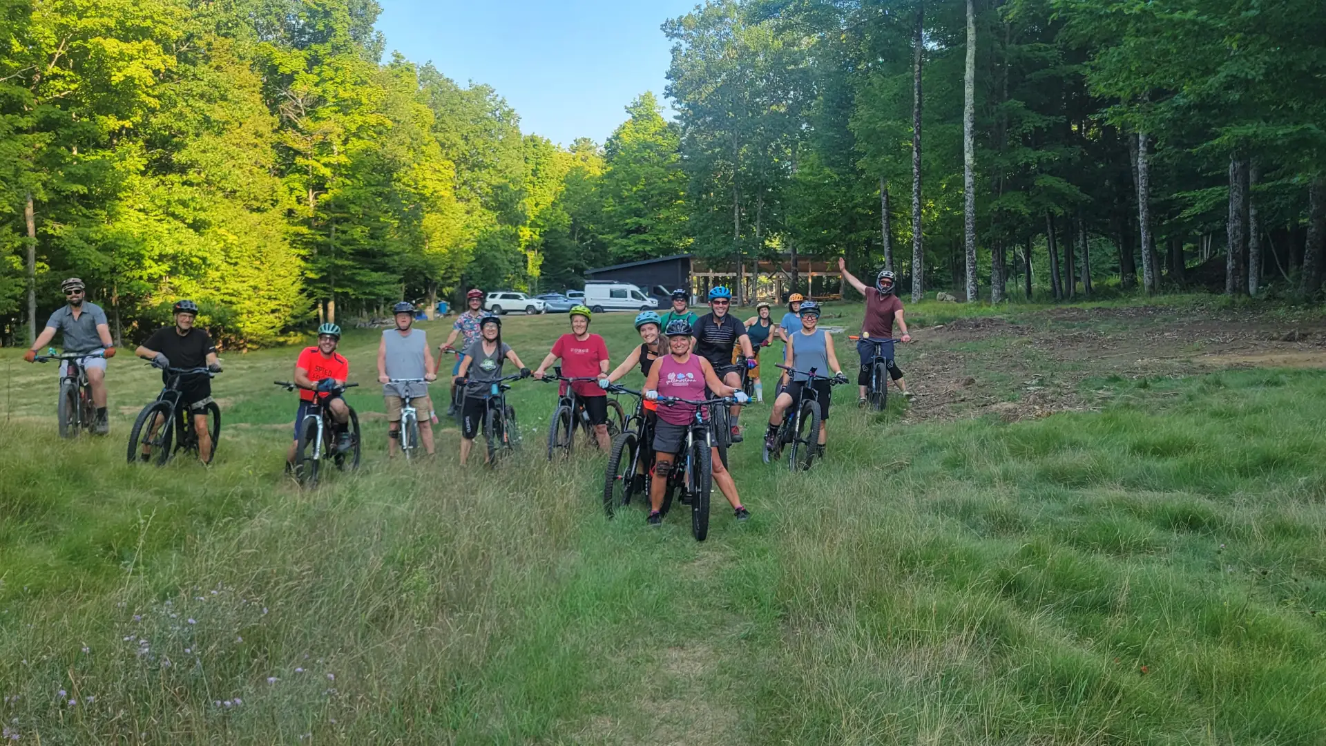 Group of mountain bikers posing together on mountain bikes on lawn surrounded by trees