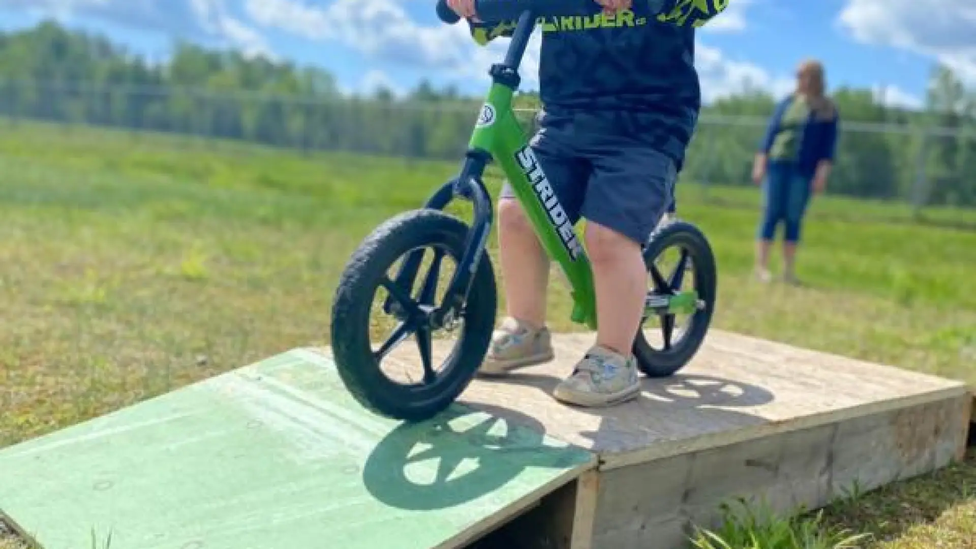 Young child on a balance bike from shoulder down. Bike is on a small ramp. 