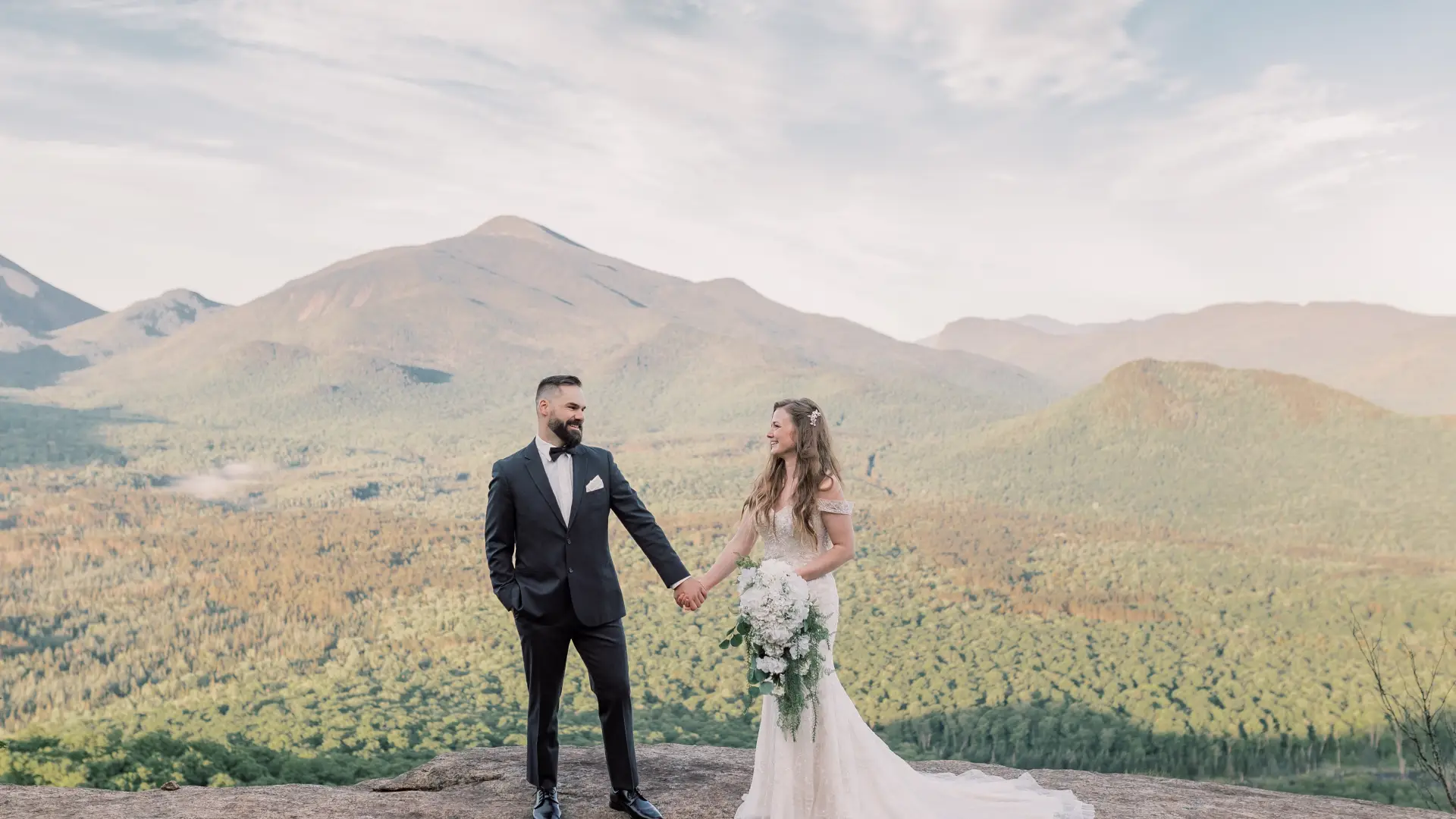 Bride and Groom gaze at each other while holding hands with mountain views in the background