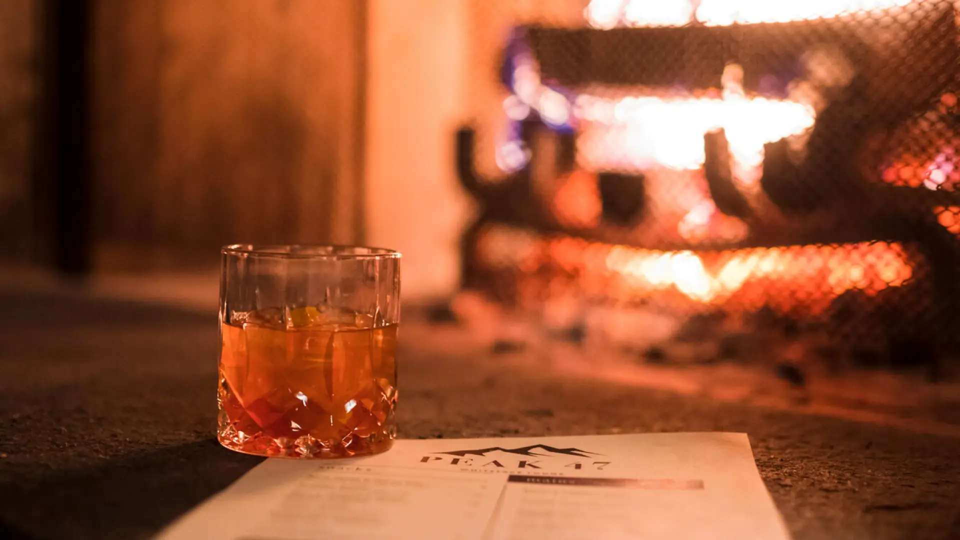 An alcoholic beverage sitting in front of a cozy fire.