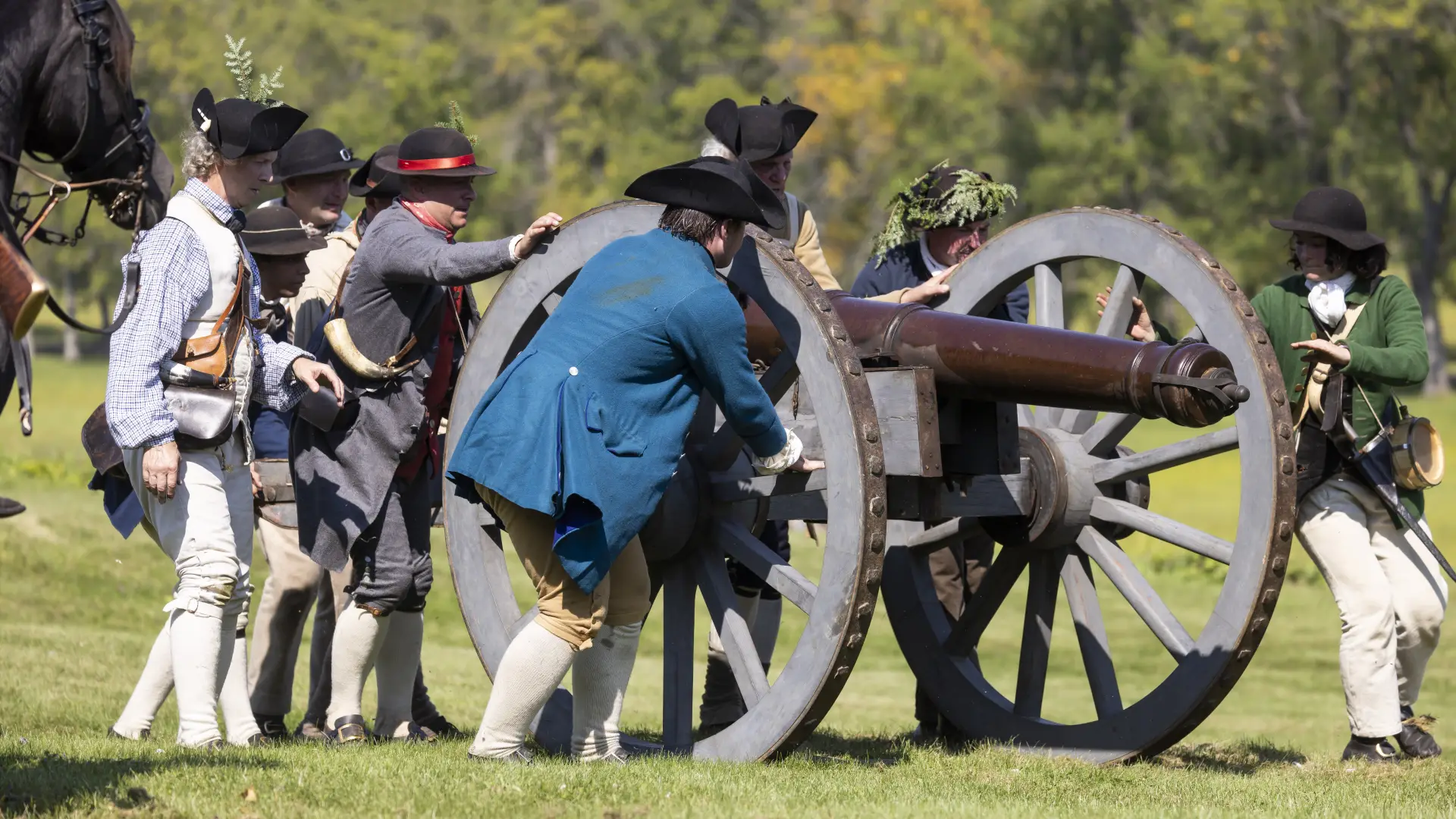 Revolutionary war reenactors move a cannon in a green field