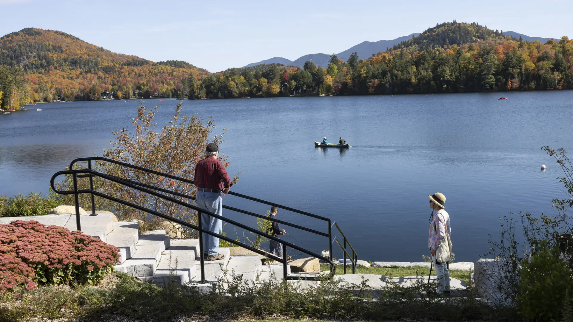 Two people watch a paddler out on a lake