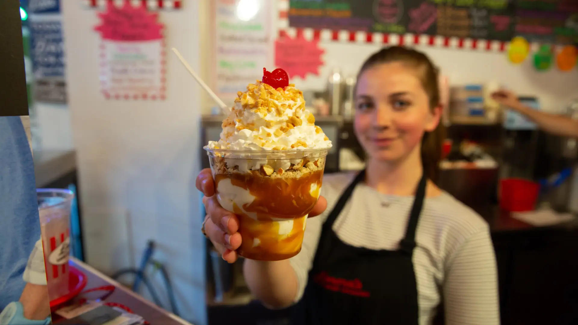 A woman holds up a caramel sundae at an ice cream shop.