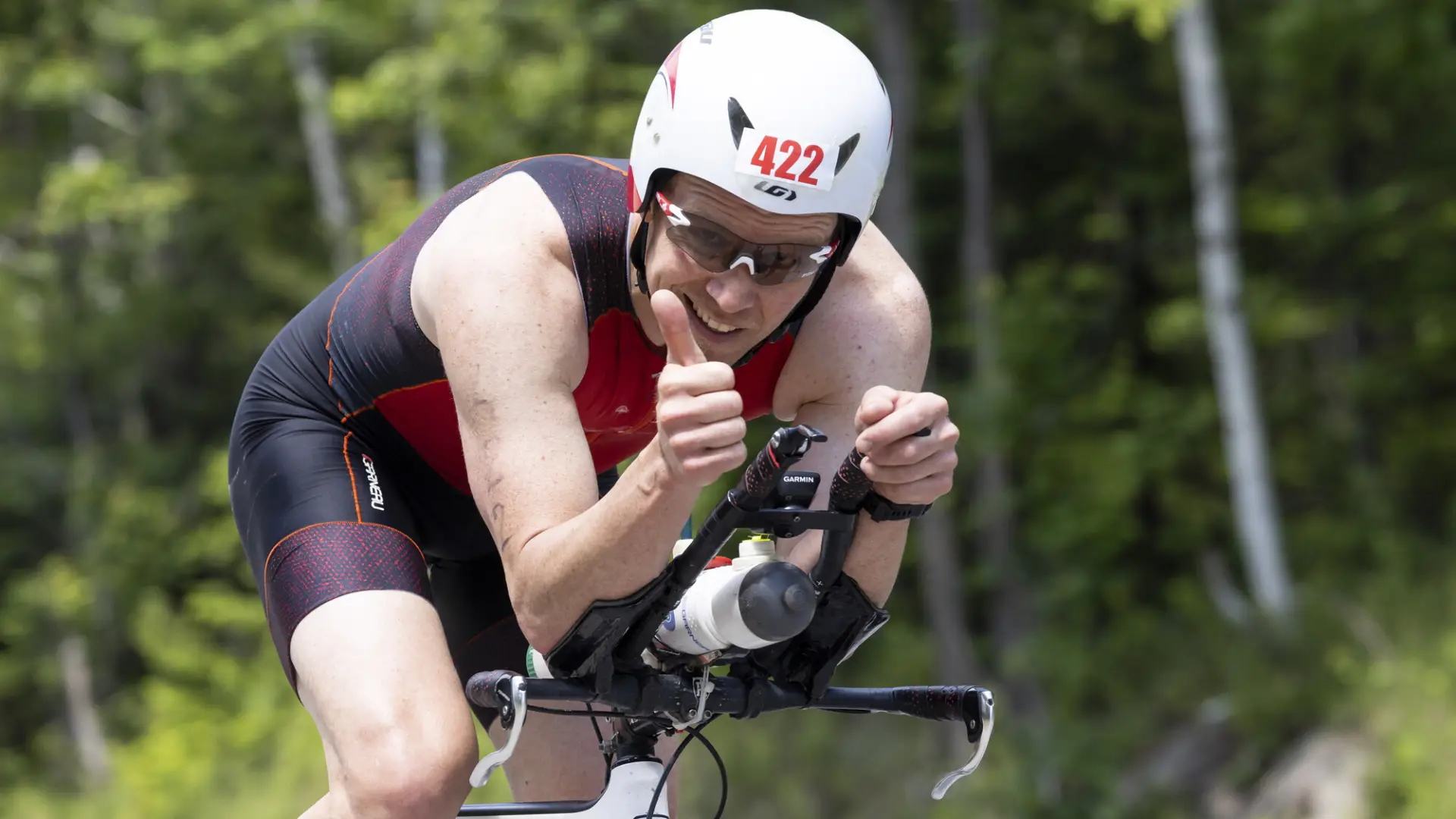 Tinman athlete give a thumbs up as they pass the camera on a bike.