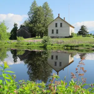 A 19th century farmhouse on a green lawn, reflected in a calm pond on a summer day.