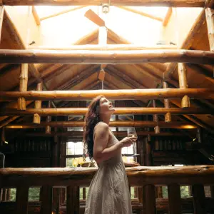 A woman stands on the balcony of a grand lodge with a glass of wine in her hand.