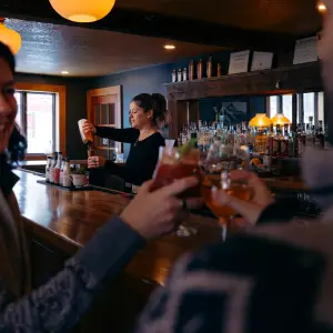 A man and woman cheers beers at a cozy bar.