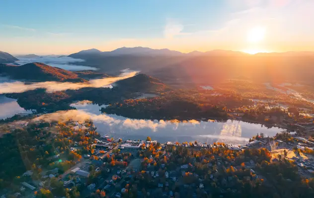 A mountain range and town tucked under clouds at dawn during fall.