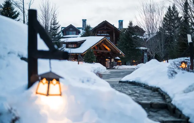 A grand lodge tucked behind heaps of snow with an icy path leading to it.