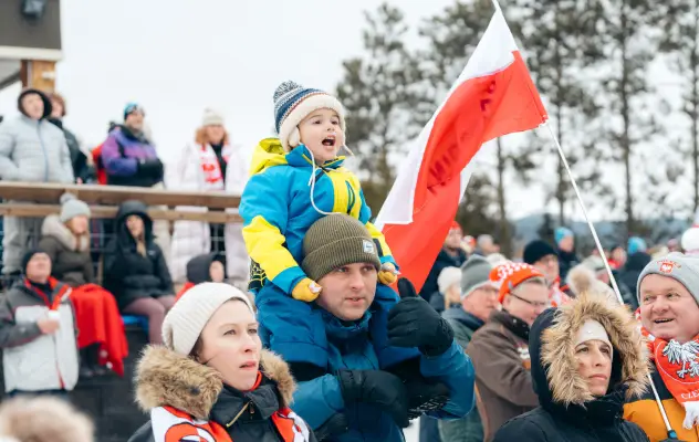 A small child sits on their dad's shoulders while watching winter sports.