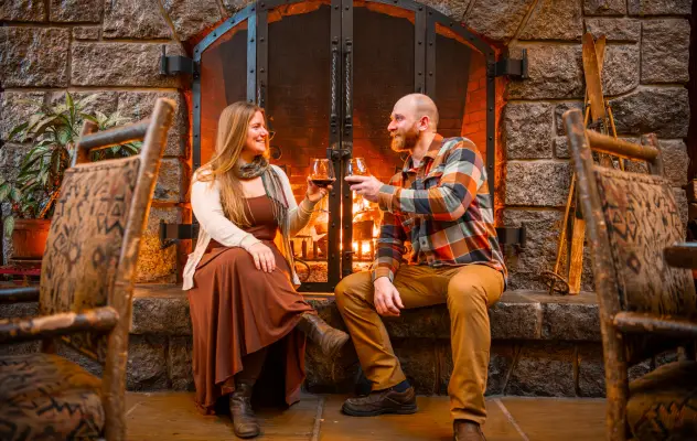 A couple sitting in front of a cozy fire with wine glasses.