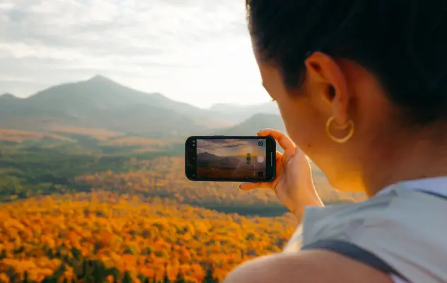 A woman takes a picture of fall mountains.