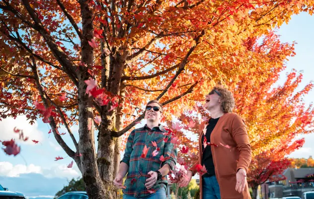A man and woman play with fall leaves in a mountain town.